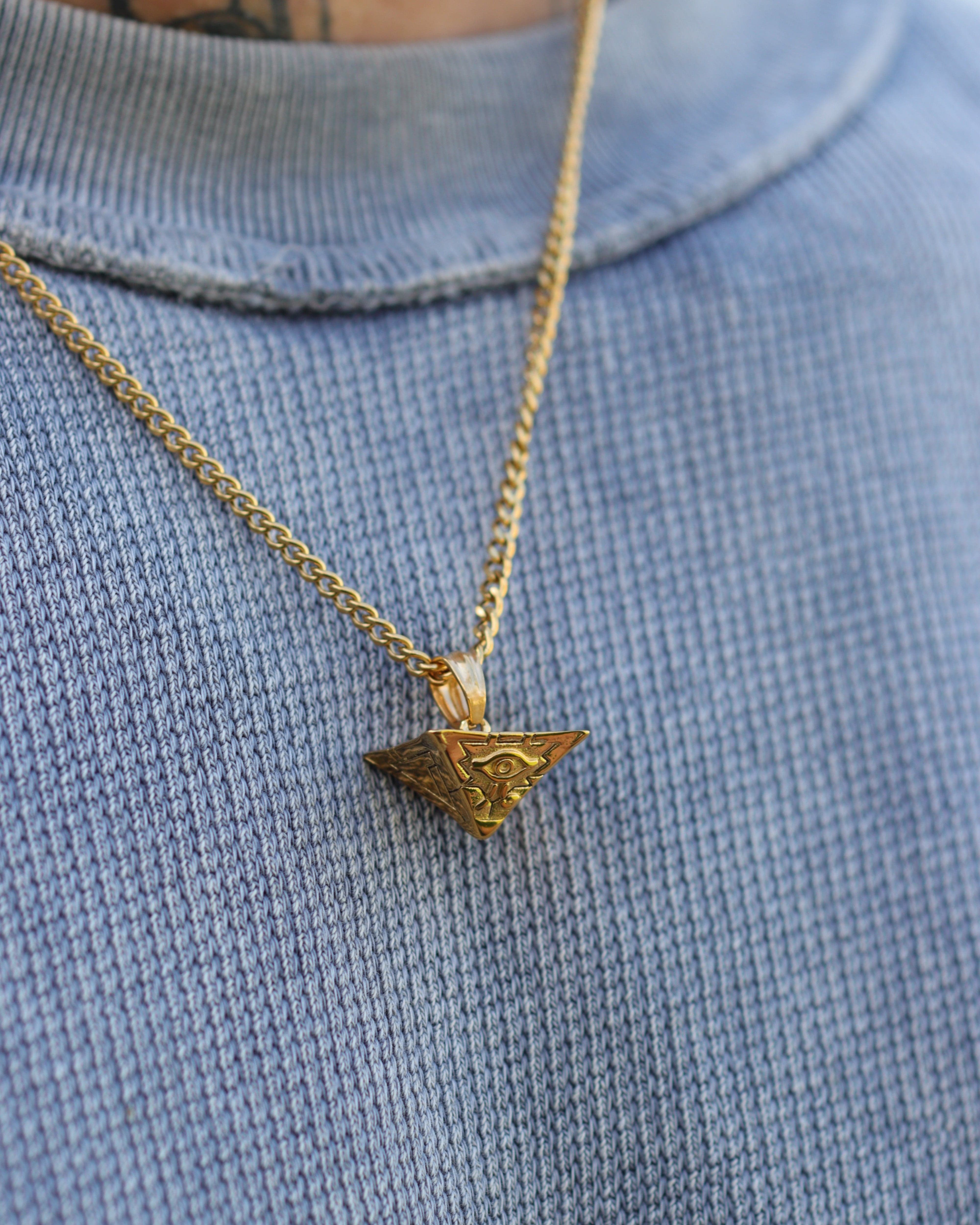 Gold necklace with a triangular pendant on a blue fabric background