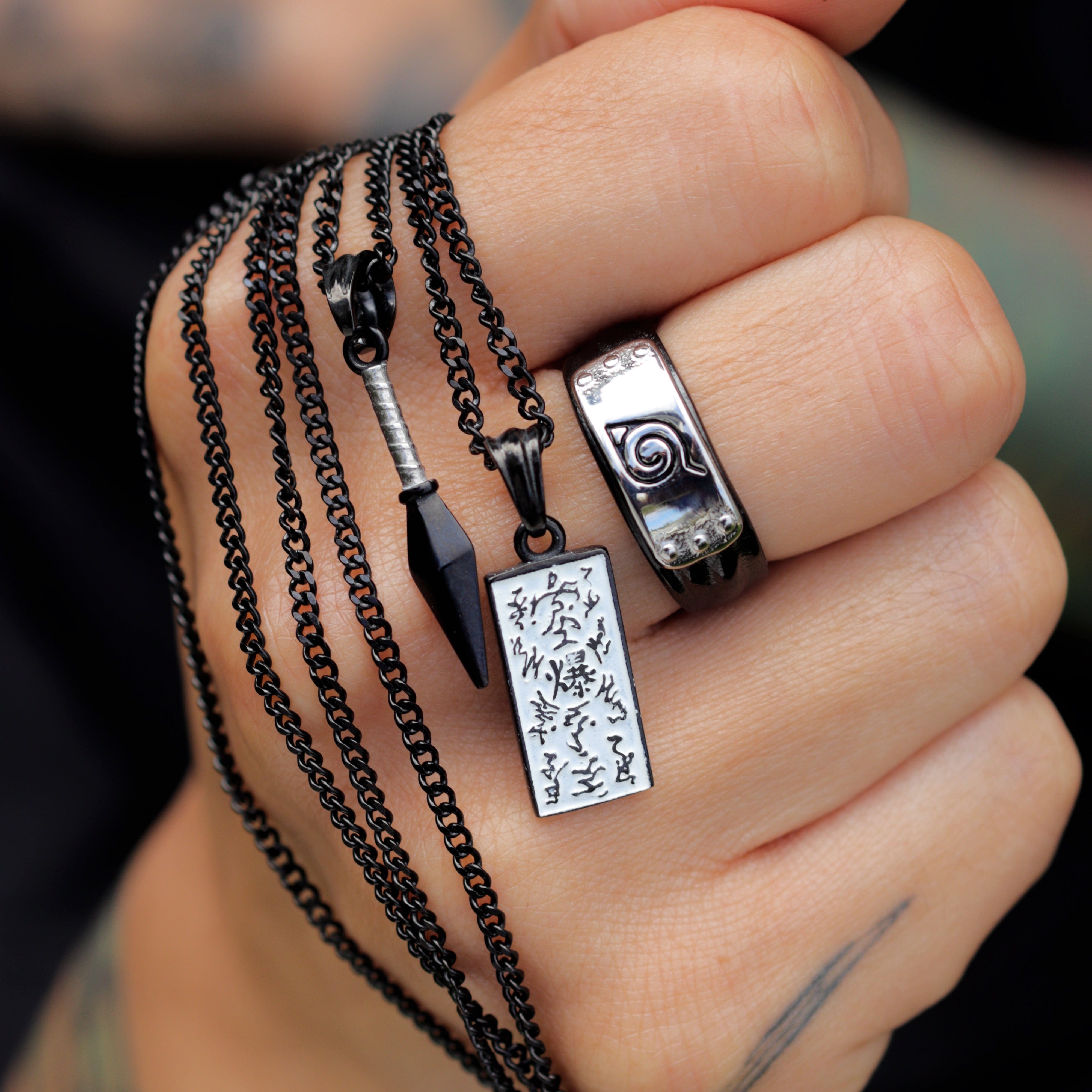 Hand wearing multiple naruto necklaces and a ring with intricate designs.