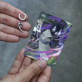 A person's hands holding a Naruto trading card featuring Sasuke Uchiha and holding a small silver crescent-shaped hoop earring next to it.