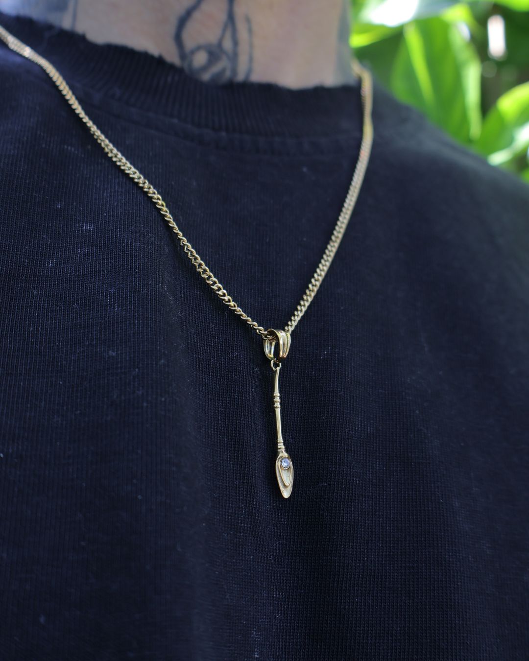 A gold chain necklace with a small pendant featuring a clear teardrop-shaped gemstone, worn on a person's neck over a dark navy blue shirt.