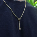A gold chain necklace with a small pendant featuring a clear teardrop-shaped gemstone, worn on a person's neck over a dark navy blue shirt.