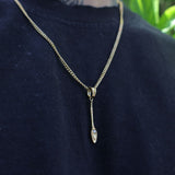 A gold chain necklace with a small pendant featuring a clear teardrop-shaped gemstone, worn on a person's neck over a dark navy blue shirt.